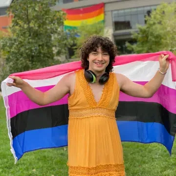 A person holding a pride flag smiles for the camera. 