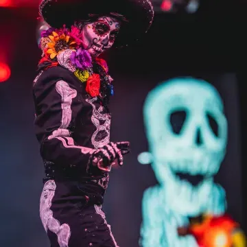 A performer on stage, dressed as el Día de los Muertos, gestures to the crowd.