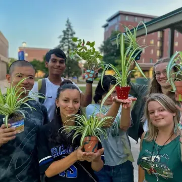 Students smile at the camera while showing off their small potted plants. 