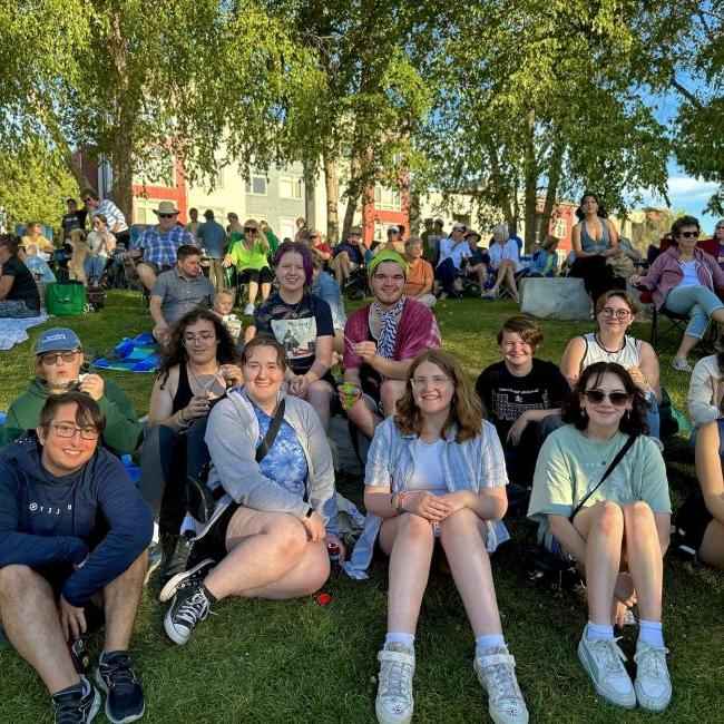 A large group of students smiles for the camera while sitting on a grassy hill.